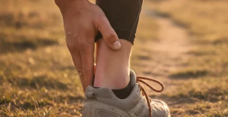 Alergător care își ține partea din spate a gleznei din cauza durerii la tendonul lui Ahile.