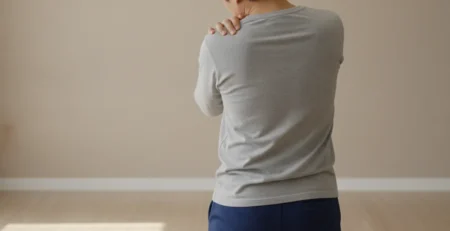 Persoană care își ține umărul dureros cu mâna, într-o cameră luminoasă